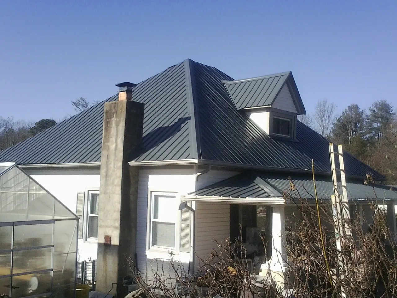 Dark blue standing seam metal roof on a white farmhouse with dormer — Slate & Tile Roof Repair by Roofing Brothers in Sharpes