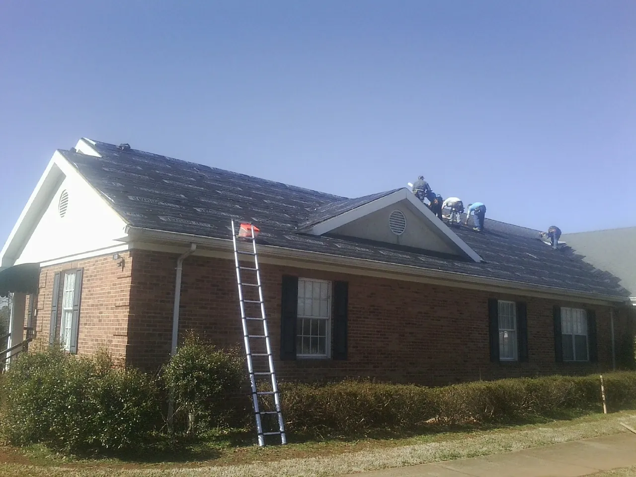 Crew tearing shingles off a brick ranch roof with a ladder set — Metal Roof Repair work by our crew in Sharpes
