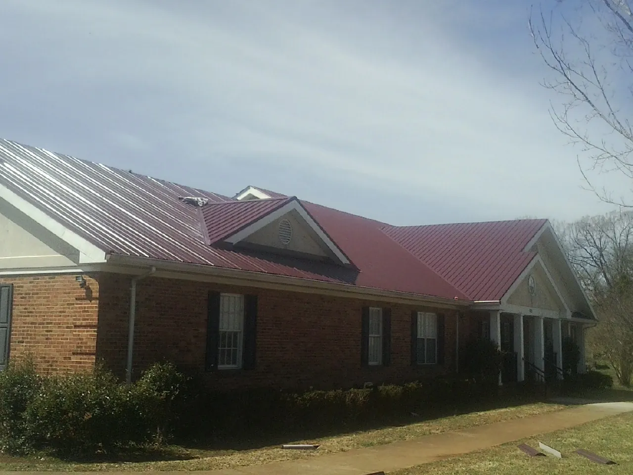 Red metal roof with gabled entries on a long brick building, from a Hail Damage Roof Repair job in Sharpes