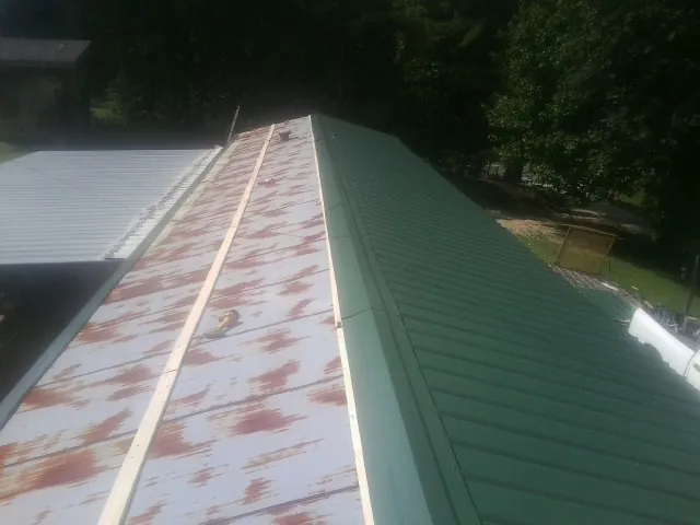 Old rusted panels beside newly installed green metal roofing — Wind Damage Roof Repair by Roofing Brothers in Sharpes