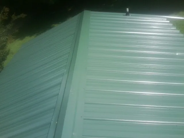 New green metal panels meeting at the ridge of a roof — Flat Roof Repair work by our crew in Sharpes