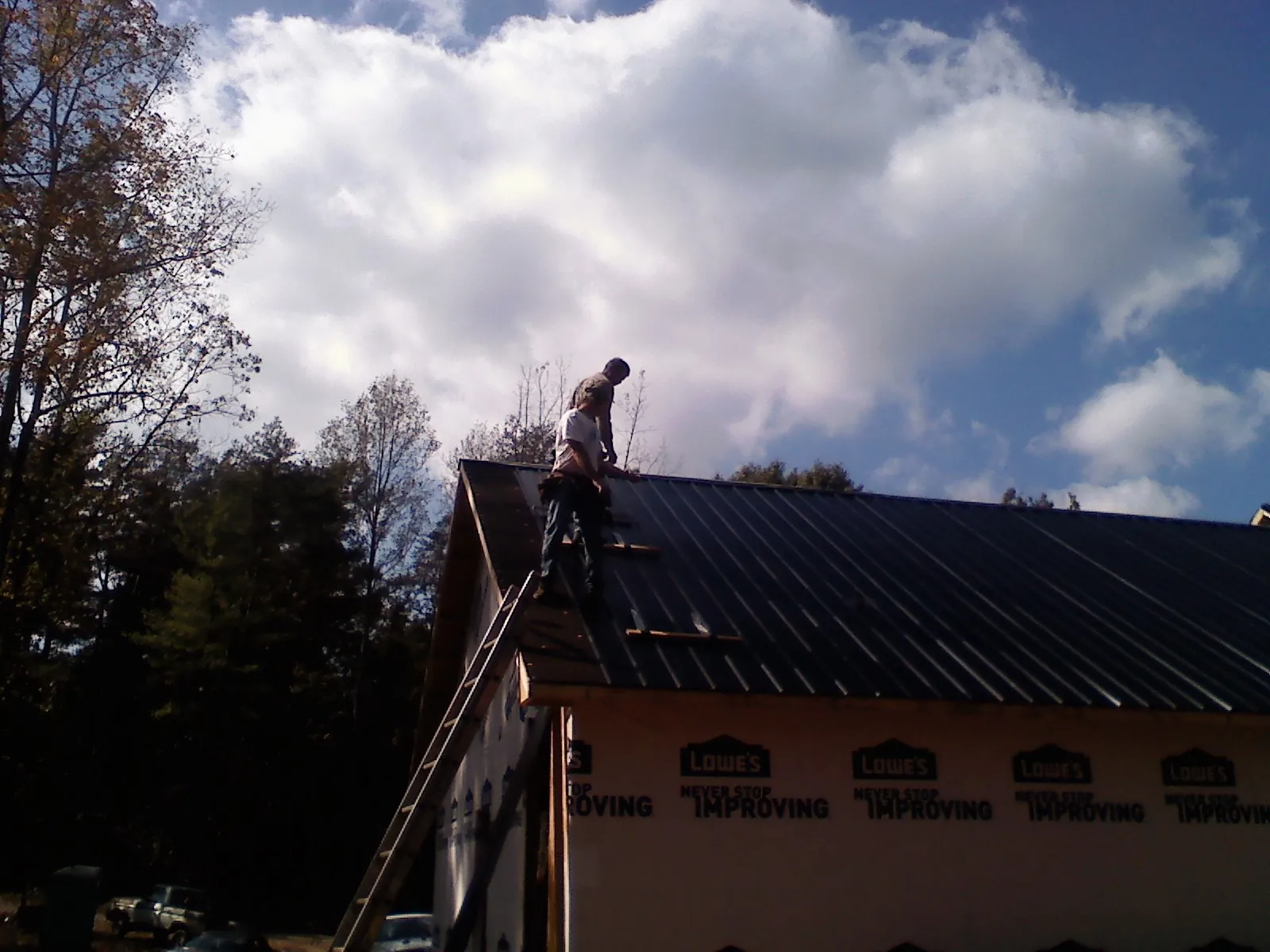 Roofer fastening dark metal panels high against a cloudy sky, from a Roof Inspection job in Sharpes