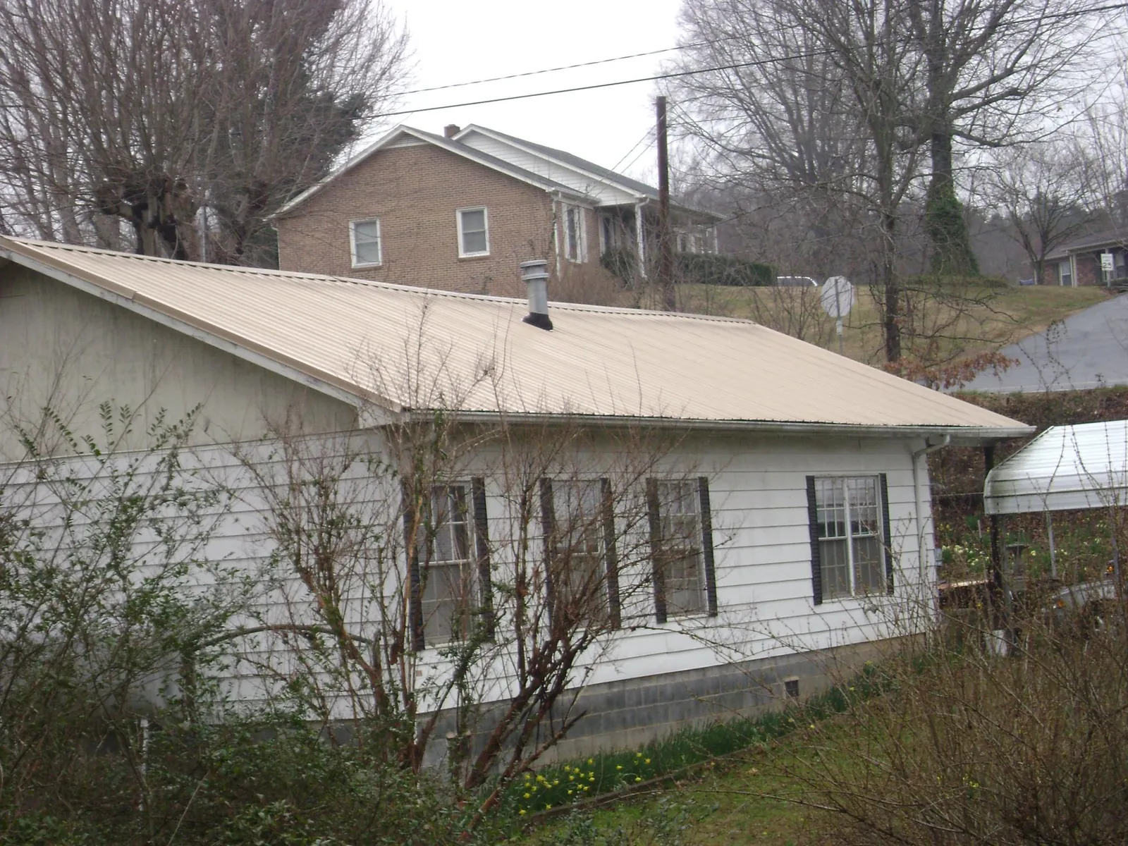 Tan metal roof on a white sided house set into a hillside — Commercial Roofing by Roofing Brothers in Sharpes
