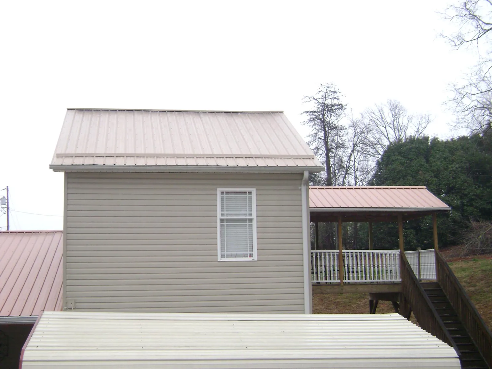Tan metal roofs on a two story addition and attached porch, from a Roof Replacement job in Sharpes